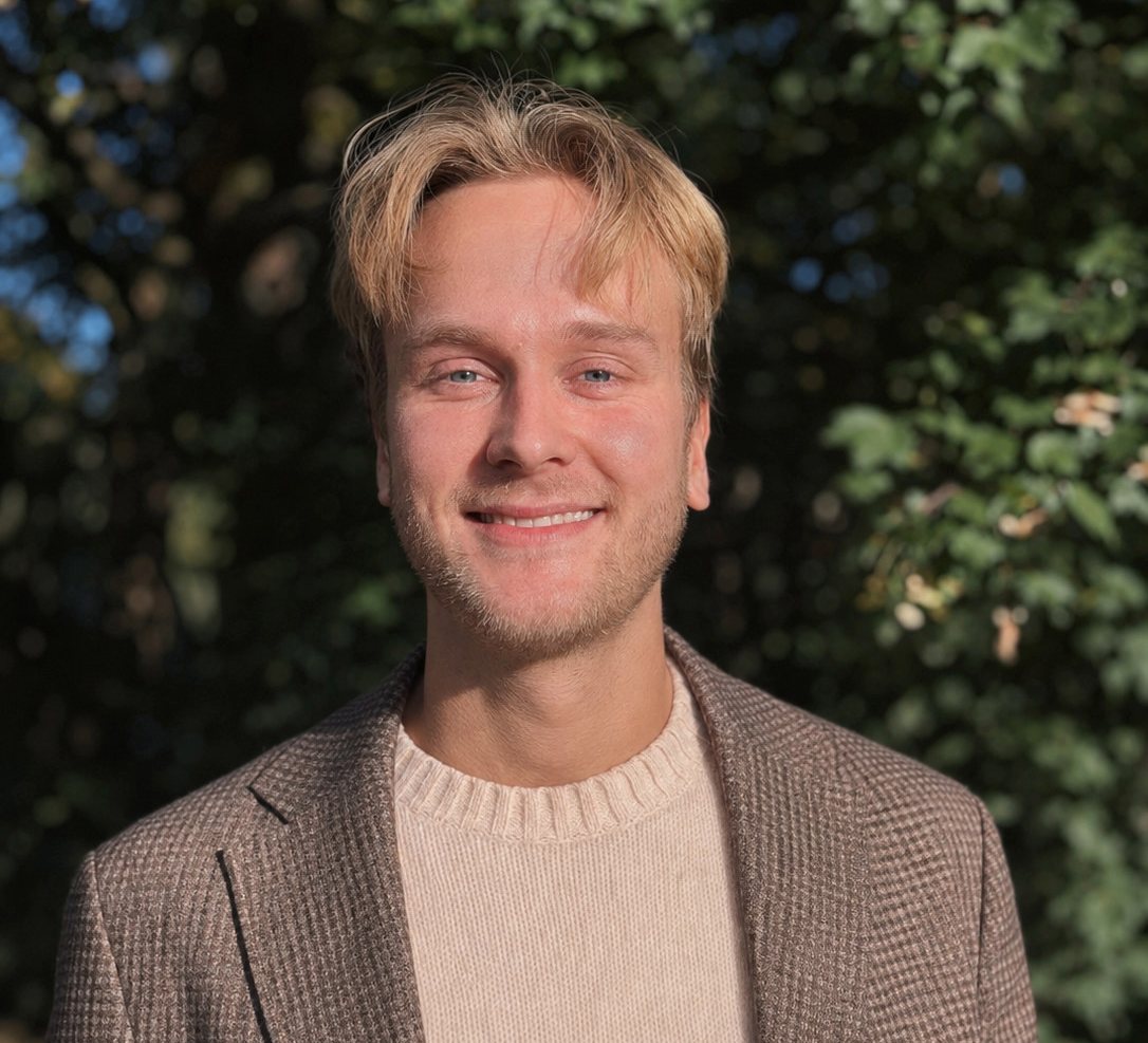 Logoped Kasper Galta smiler i høstsol foran grønt løvverk